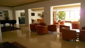 A spacious living room with a piano, multiple orange armchairs, and a large window providing natural light.