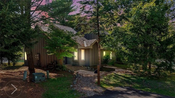 A small, single-story wooden cabin with a sloped roof, surrounded by trees and a gravel path leading to the entrance.