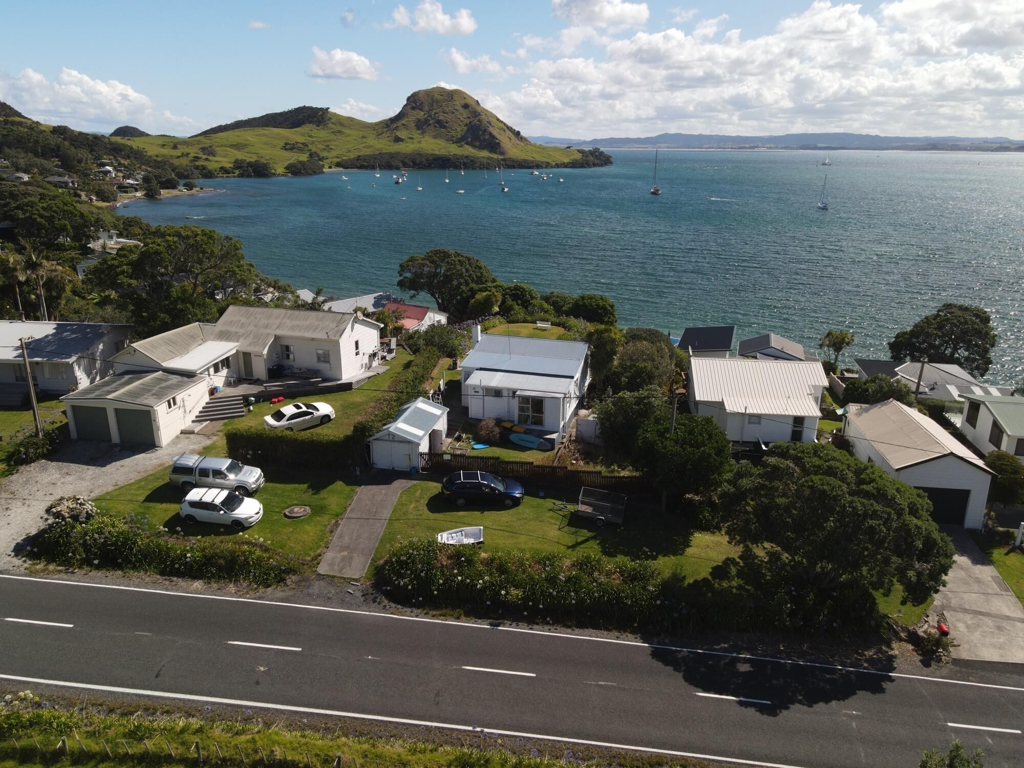 Un área residencial costera con casas, una calle y vistas al mar con barcos.