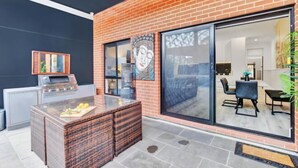 An outdoor patio with a brick wall, a glass door leading inside, a grill, and a seating area with a table and chairs. - Noir Cottage Glenelg North 3Br Netflix BBQ (Glenelg North)