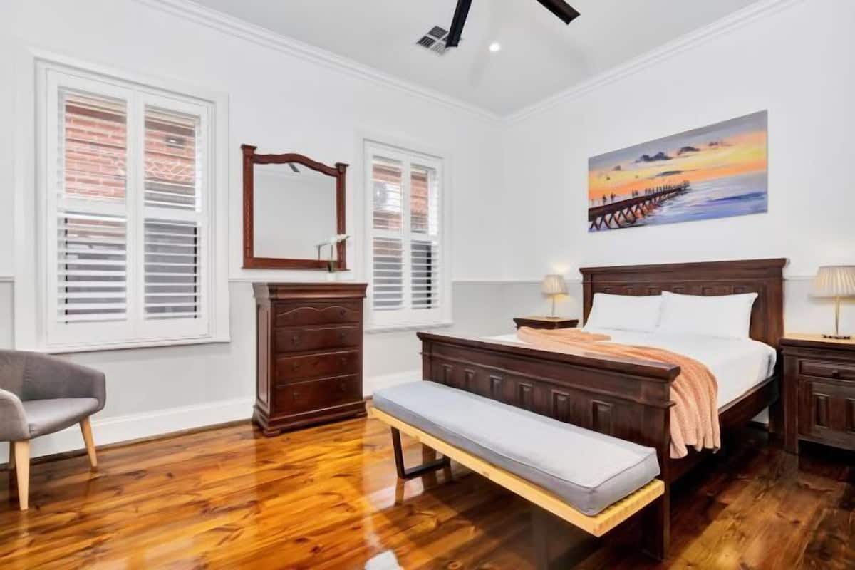 A bedroom with a wooden bed, a bench, a dresser, a chair, and a painting on the wall.