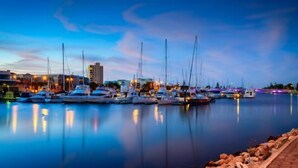 A marina at dusk with multiple sailboats docked, calm water, and buildings in the background. - Noir Cottage Glenelg North 3Br Netflix BBQ (Glenelg North)