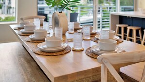 A dining table set with white plates, bowls, and glasses, with a wooden chair and a potted plant in the background. - Keys Casa: Elegant Waterfront Retreat, Sleeps 16, Elevator, Private Dock, Putt-Putt (Key Largo)