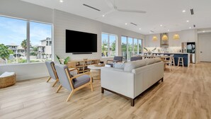 A spacious living room with a large TV, comfortable seating, and a view of the outside. - Keys Casa: Elegant Waterfront Retreat, Sleeps 16, Elevator, Private Dock, Putt-Putt (Key Largo)