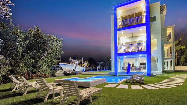 A modern multi-story building with a pool and outdoor seating area. - Keys Casa: Elegant Waterfront Retreat, Sleeps 16, Elevator, Private Dock, Putt-Putt (Key Largo)