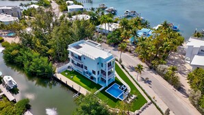 A modern two-story house with a swimming pool, surrounded by lush greenery and a marina. - Keys Casa: Elegant Waterfront Retreat, Sleeps 16, Elevator, Private Dock, Putt-Putt (Key Largo)