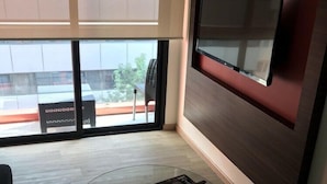 A modern living room with a glass coffee table, a flat-screen TV mounted on the wall, and a view of the outside through large windows. - Mc Suites Reforma (Mexico City)