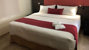 A neatly made bed with white and red bedding, a red pillow, and a white towel on the bed. - Mc Suites Reforma (Mexico City)