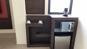 A compact kitchenette with a built-in microwave and refrigerator, two white cups on a shelf, and a coffee maker on the countertop. - Mc Suites Reforma (Mexico City)