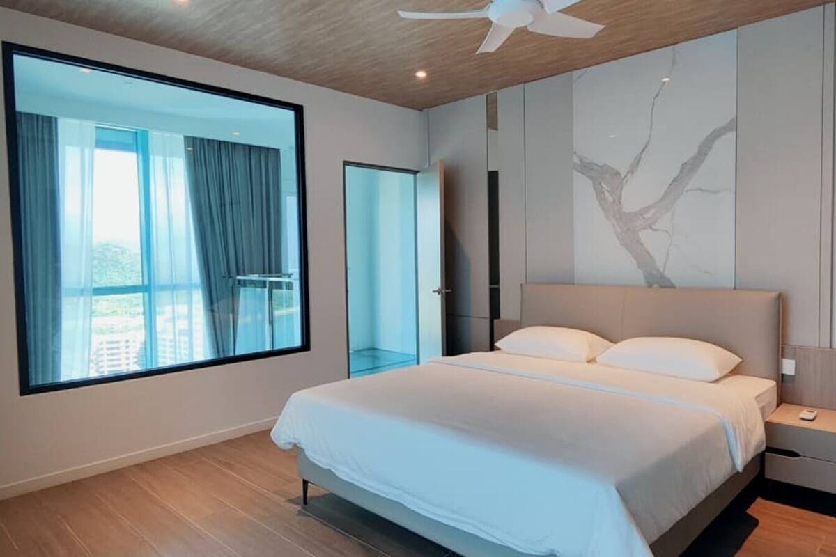 A modern bedroom with a large bed, a ceiling fan, a large window with curtains, and a tree mural on the wall.