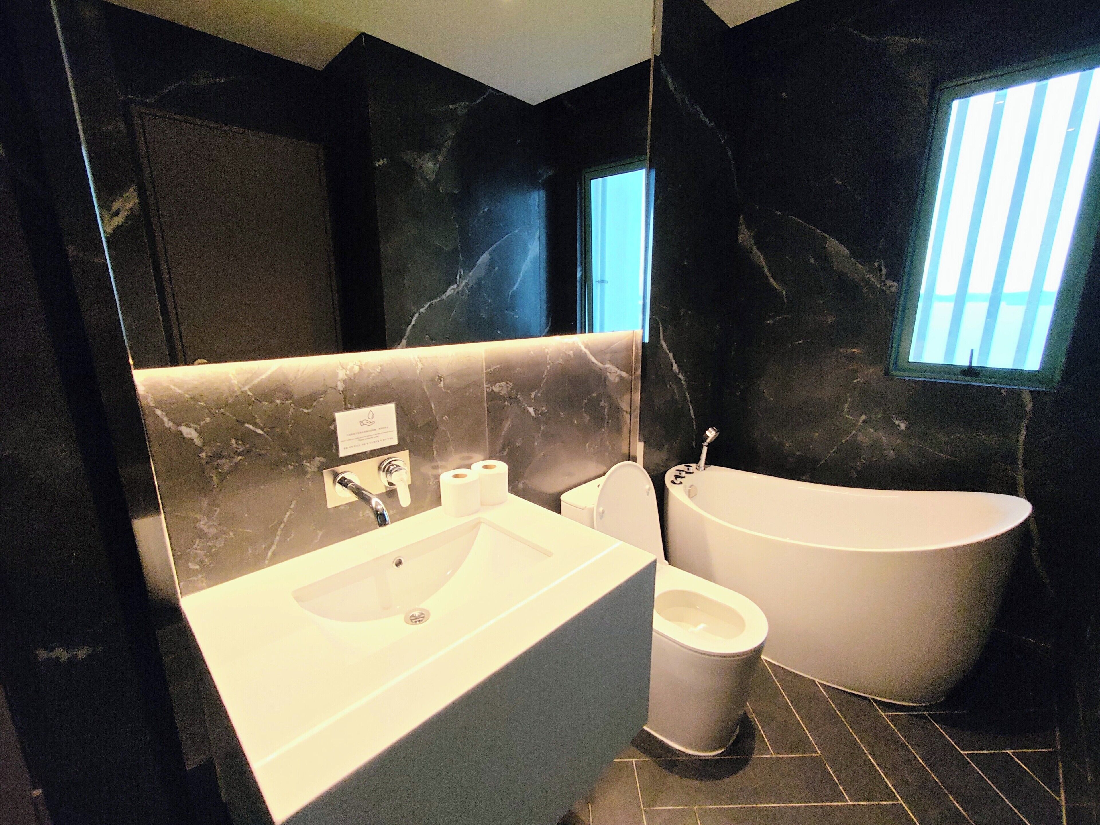 A modern bathroom with a marble vanity, a toilet, and a freestanding bathtub.