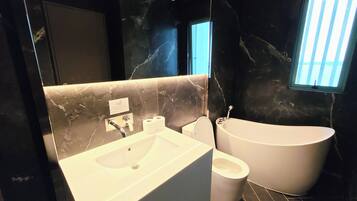 A modern bathroom with a marble vanity, a toilet, and a freestanding bathtub.