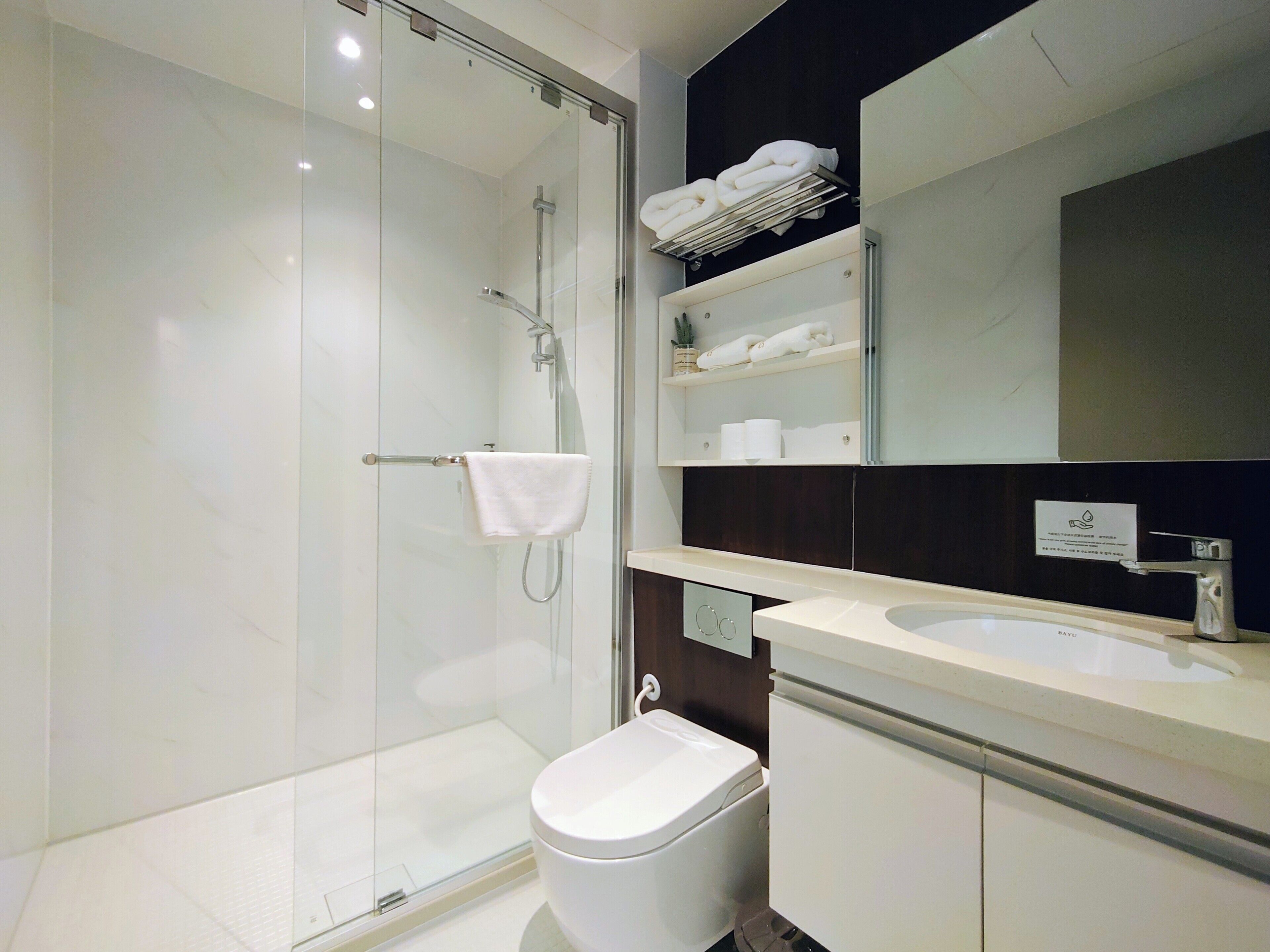 Un baño moderno con cabina de ducha de vidrio, inodoro blanco, lavabo y espejo sobre el lavabo.