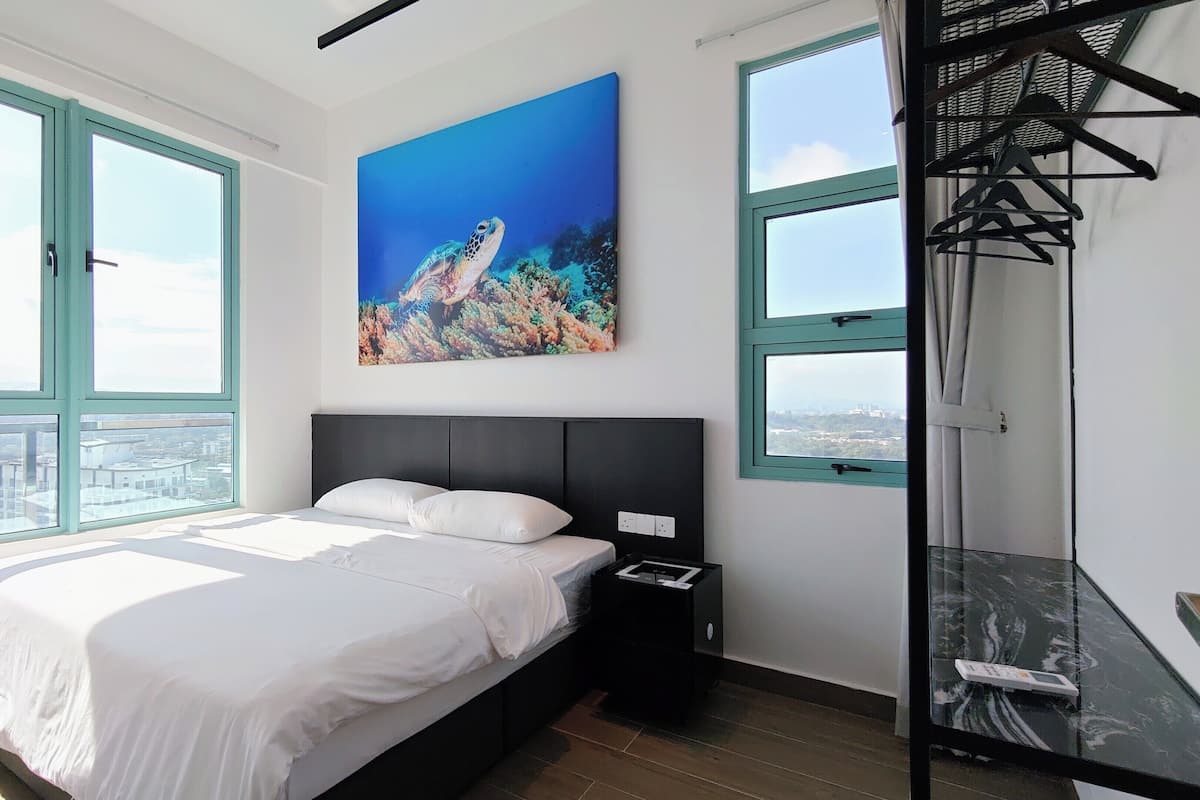 A modern bedroom with a large bed, a painting of a sea turtle, and a city view through the windows.
