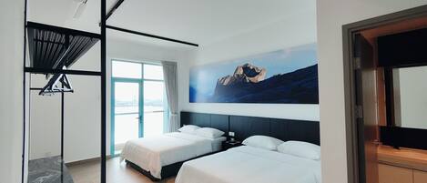 Una habitación de hotel moderna con dos camas, un ventanal grande, un cuadro de montañas y un espejo con marco negro.