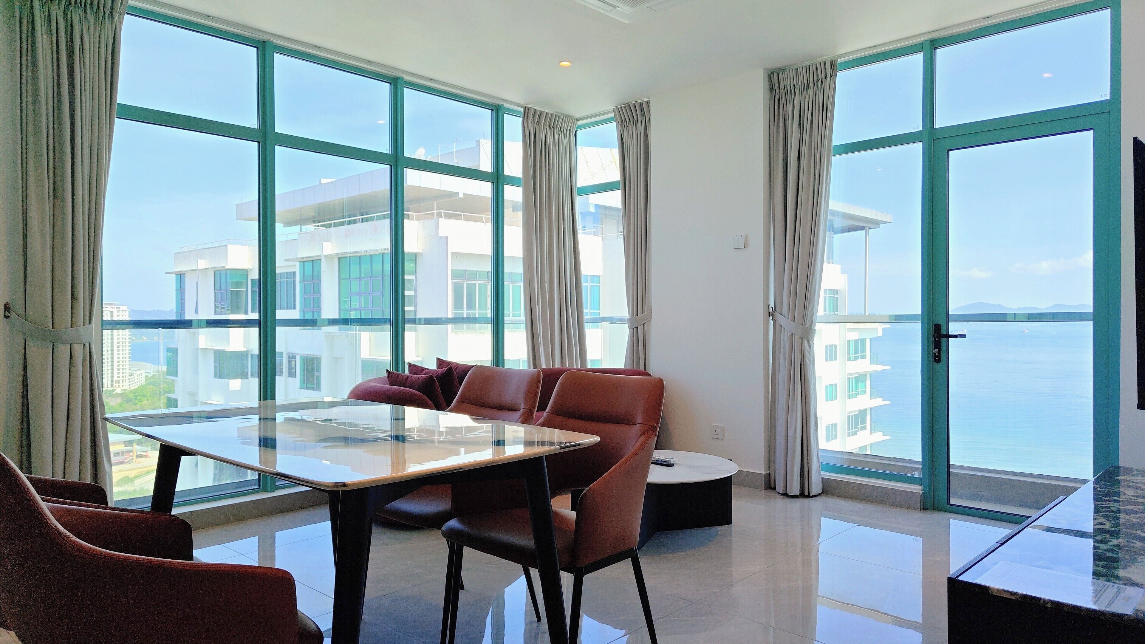 A modern hotel room with a large balcony, a dining table, and comfortable seating.