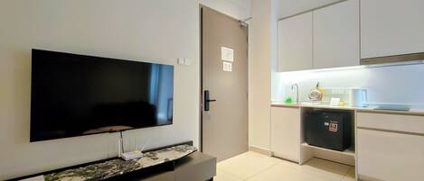 Una sala de estar moderna con un televisor de pantalla plana montado en la pared, una mesa de centro con diseño de mármol y una pequeña cocina con refrigerador y pileta.