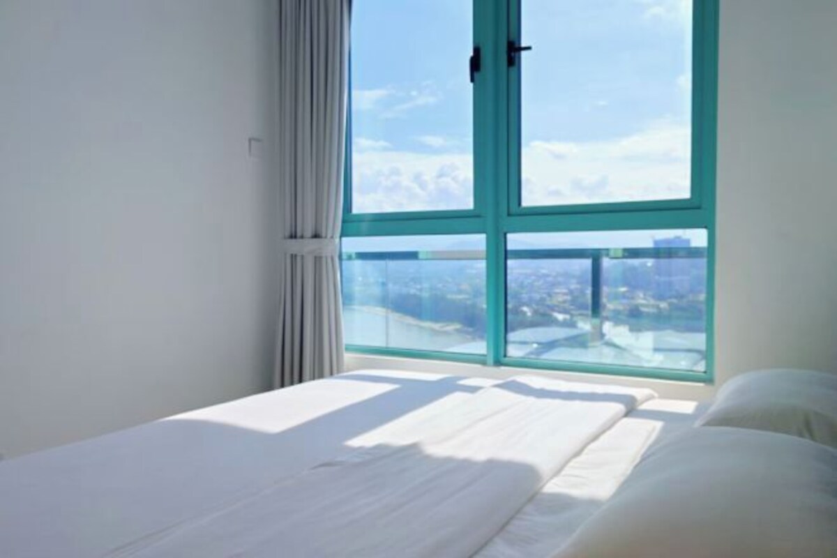 A room with a bed, a window with curtains, and a view of a cityscape.
