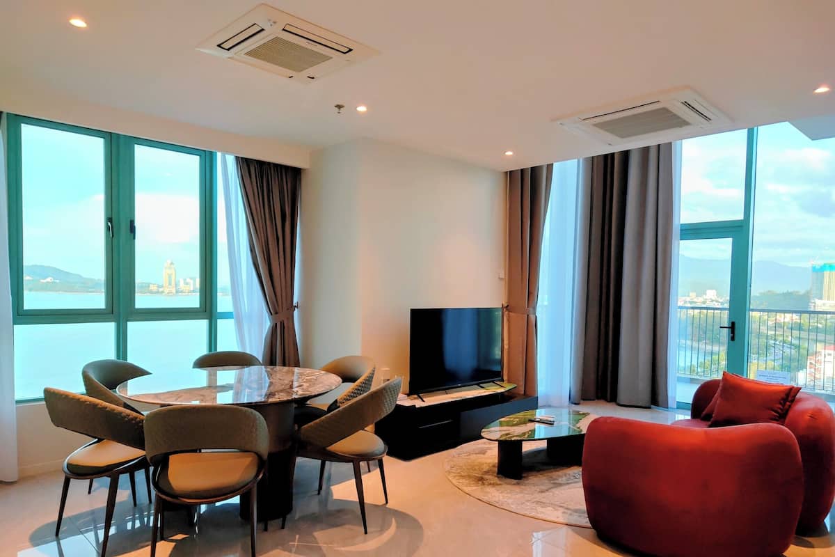 A modern living room with a round dining table, comfortable seating, a flat-screen TV, and large windows offering a city view.