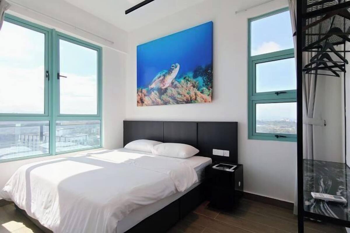 A bedroom with a bed, a nightstand, a painting, and large windows.