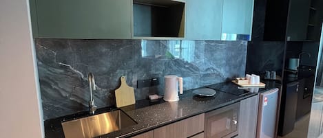 A modern kitchen with dark green cabinets, a marble backsplash, and stainless steel appliances.