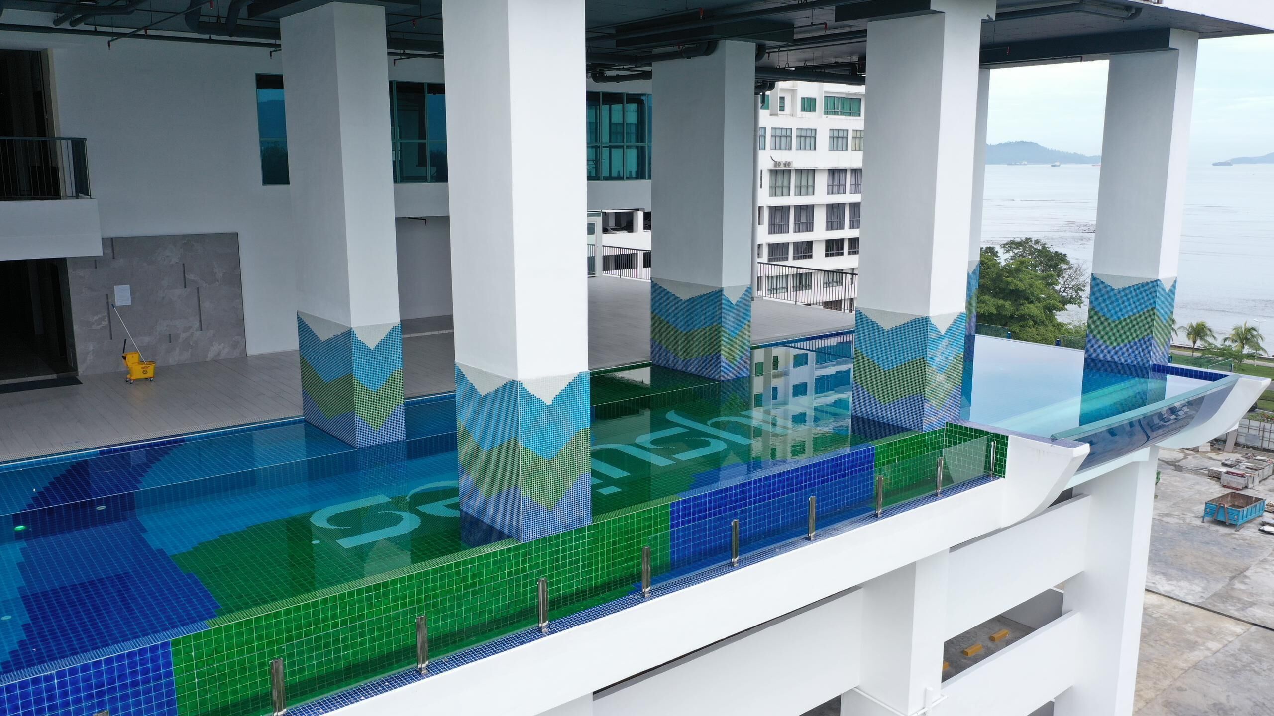 A modern building with a glass-bottomed pool, white pillars, and a view of the sea.