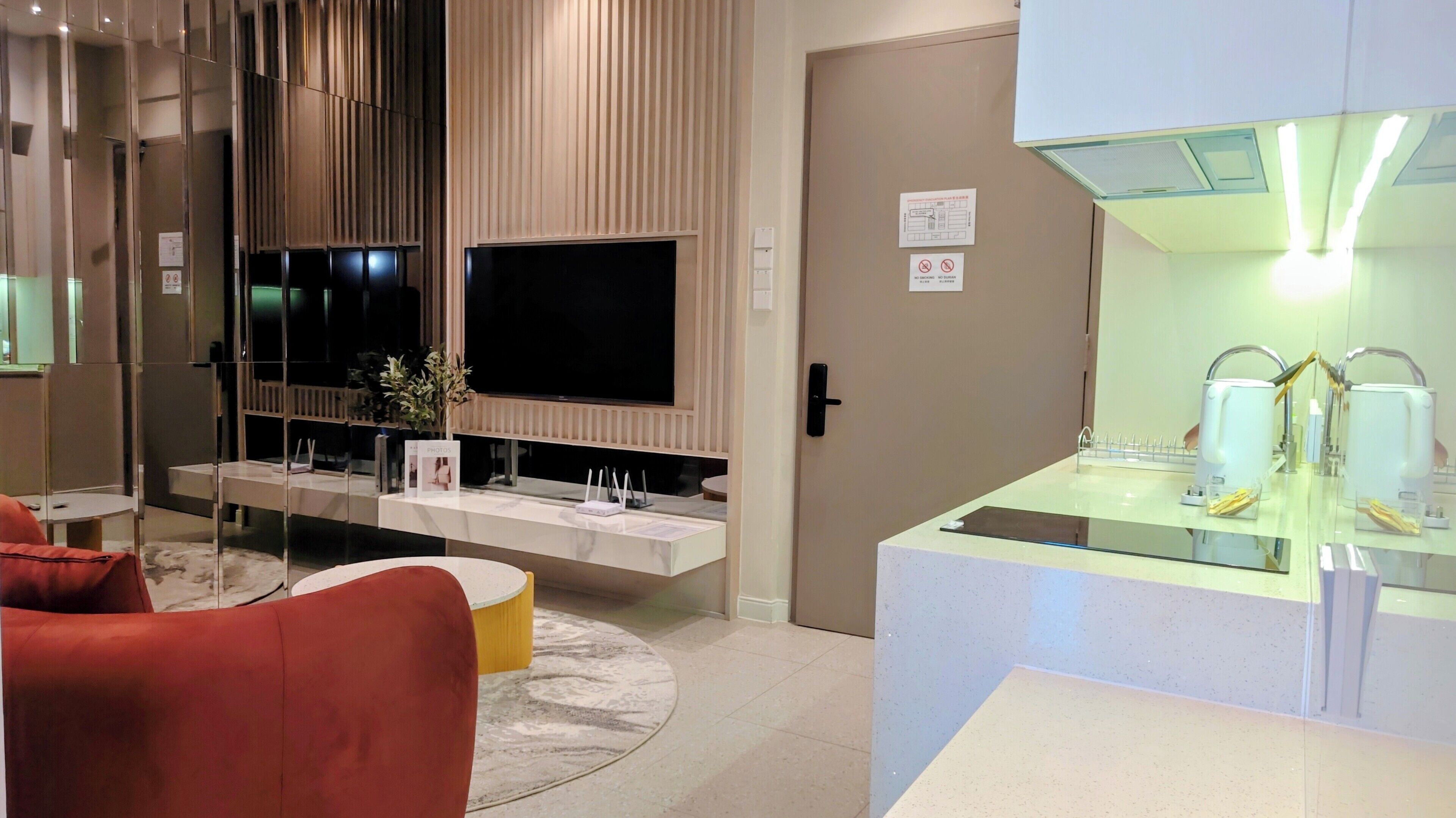 A modern hotel room with a flat-screen TV, a glass shower enclosure, a sofa, and a small table with a vase of flowers.