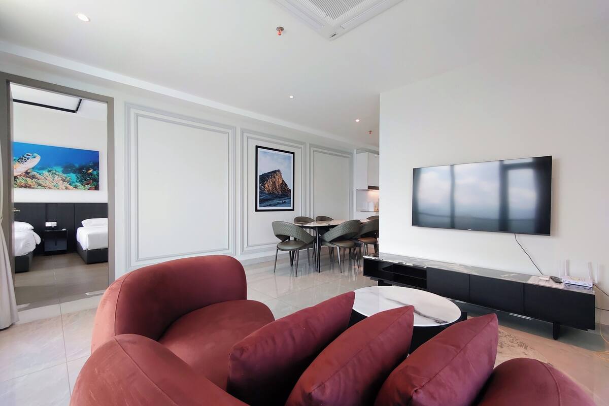 A modern living room with a large flat-screen TV, a red sofa, and a dining area with chairs and a table.