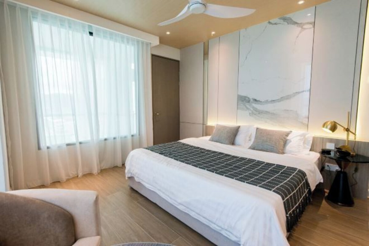 A modern hotel room with a large bed, a ceiling fan, and a marble wall.