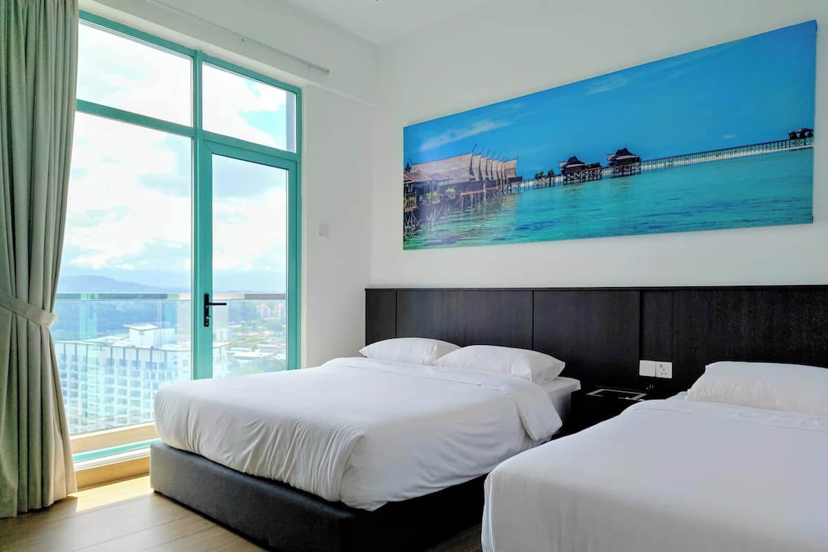 A hotel room with two beds, a large window with a view of the city, and a painting of a coastal scene.