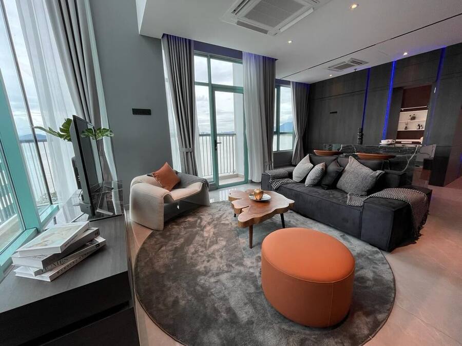 A modern living room with a sofa, ottoman, and coffee table, large windows with curtains, and a view of the city.