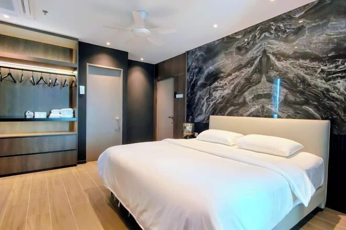 A modern hotel room with a large bed, a ceiling fan, a marble wall mural, and a wardrobe with hanging clothes.