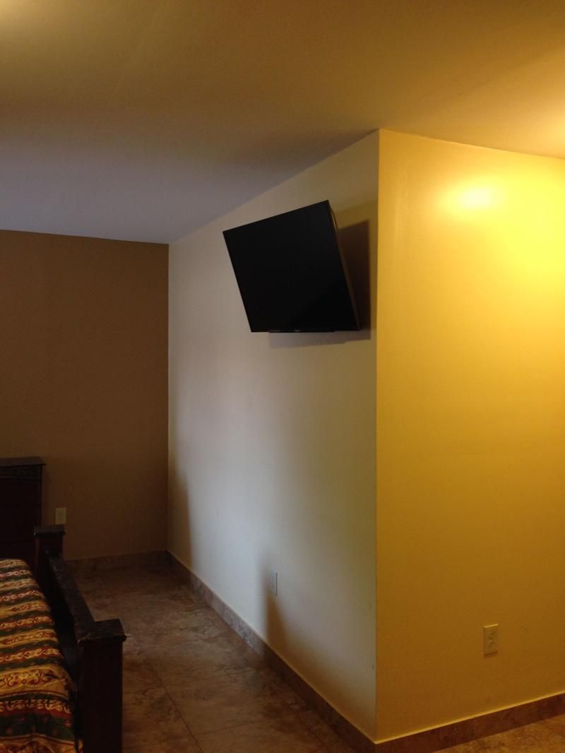 A room with a bed, a small table, and a TV mounted on the wall.