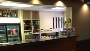 A reception area with a counter, shelves with various items, a refrigerator, and a red carpet. - Miami Princess Hotel (Miami)