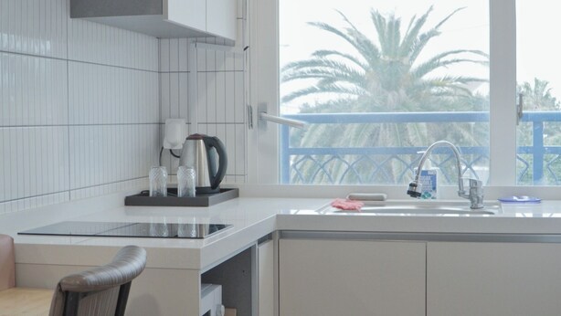 Una cocina moderna con armarios blancos, un hervidor de acero inoxidable y una ventana con vistas a palmeras.