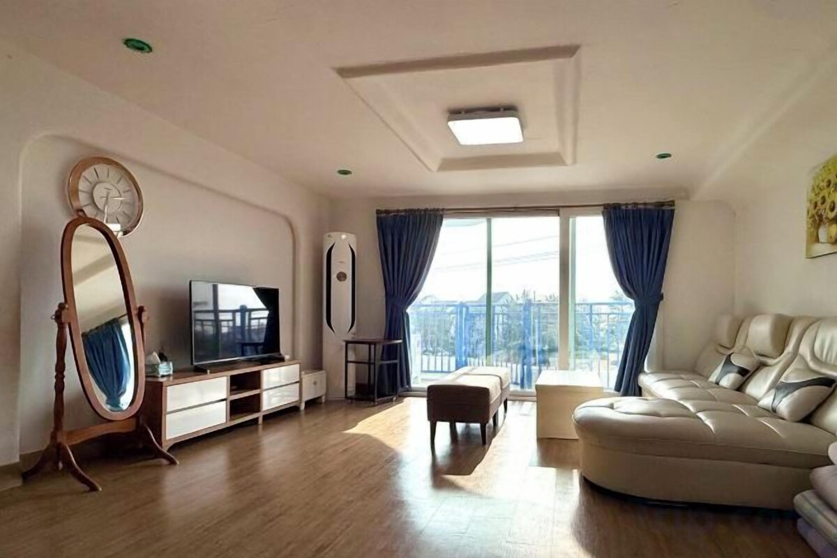 Un salon avec un canapé, un téléviseur, un miroir et une fenêtre avec des rideaux.