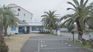 A building with a white exterior and blue accents, a parking area with EV charging stations, and palm trees. - Sweet Stay (Seogwipo)