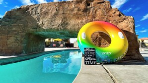 A swimming pool with a rainbow inflatable ring, a sign reading "Relax You're in River Time", and a large rock formation in the background. - Red Rock Roamin' | Private Pool, & Hot Tub | Resort Amenities | Sleeps 21 (Hurricane)