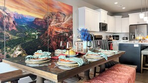 A modern kitchen with white cabinets, a large island, and a dining table set for a meal. - Red Rock Roamin' | Private Pool, & Hot Tub | Resort Amenities | Sleeps 21 (Hurricane)