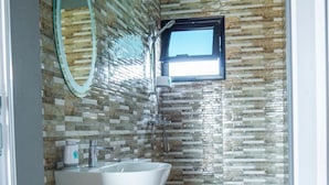 Modernilla designilla varustettu kylpyhuone, jossa on kivimosaiikkiseinä, suuri peili, pesuallas, wc ja suihku.