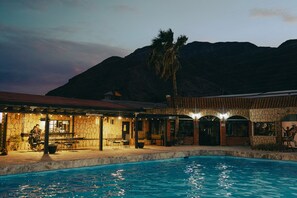 Zona de piscina con un edificio de piedra y una montaña al fondo.