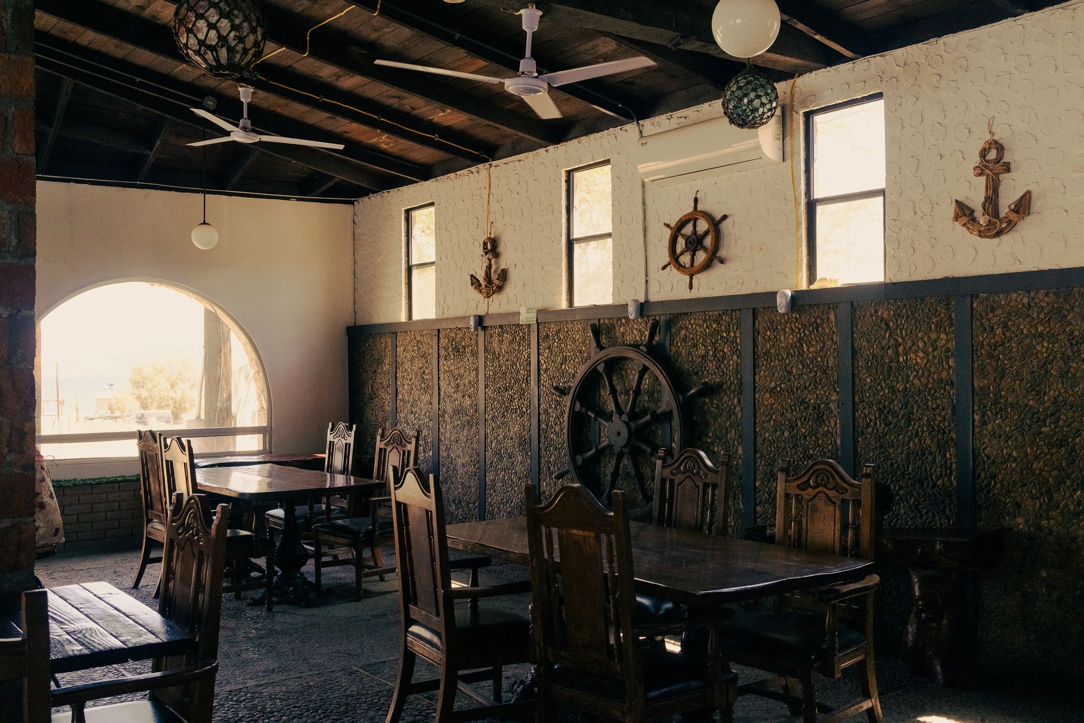 A dining area with wooden tables and chairs, nautical-themed wall decorations, and a large window providing natural light.