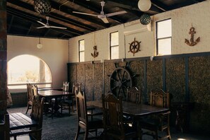A dining area with wooden tables and chairs, nautical-themed wall decorations, and a large window providing natural light.