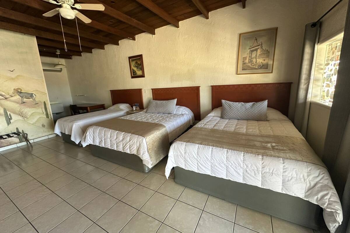A hotel room with two beds, a ceiling fan, a mural, and a framed picture on the wall.