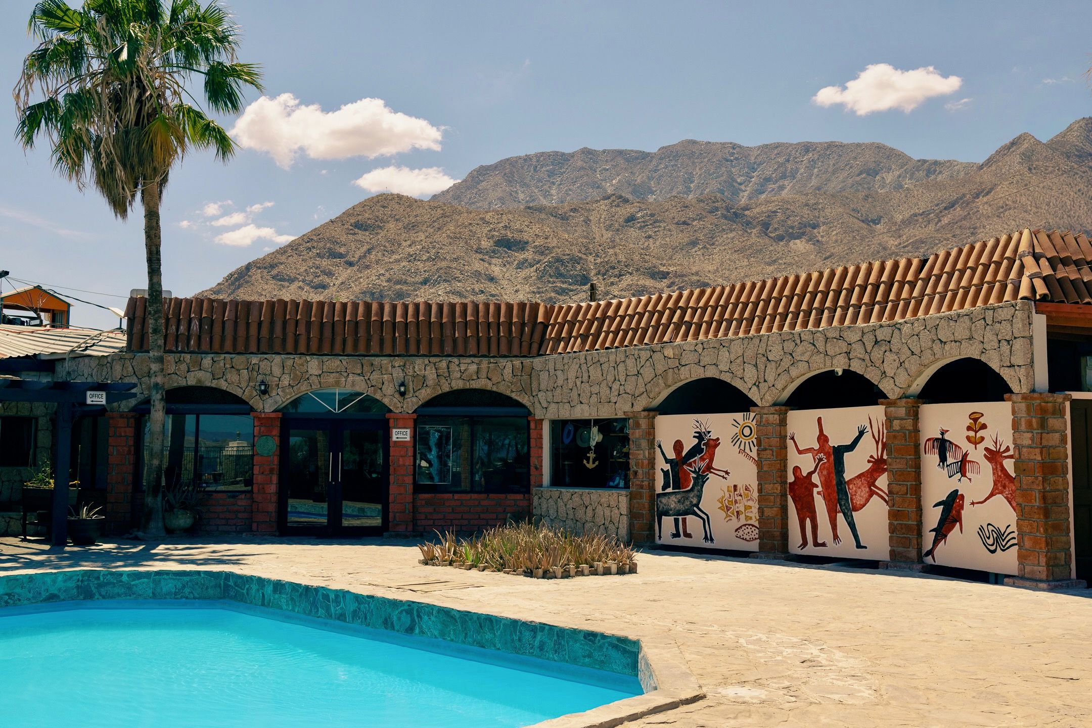 A building with a pool, office signs, and a mural with indigenous art.