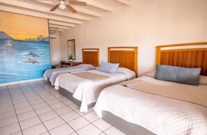 A hotel room with three beds, a ceiling fan, a mural of dolphins, and a tiled floor. - Hotel Villa Vitta (Bahia de los Angeles)