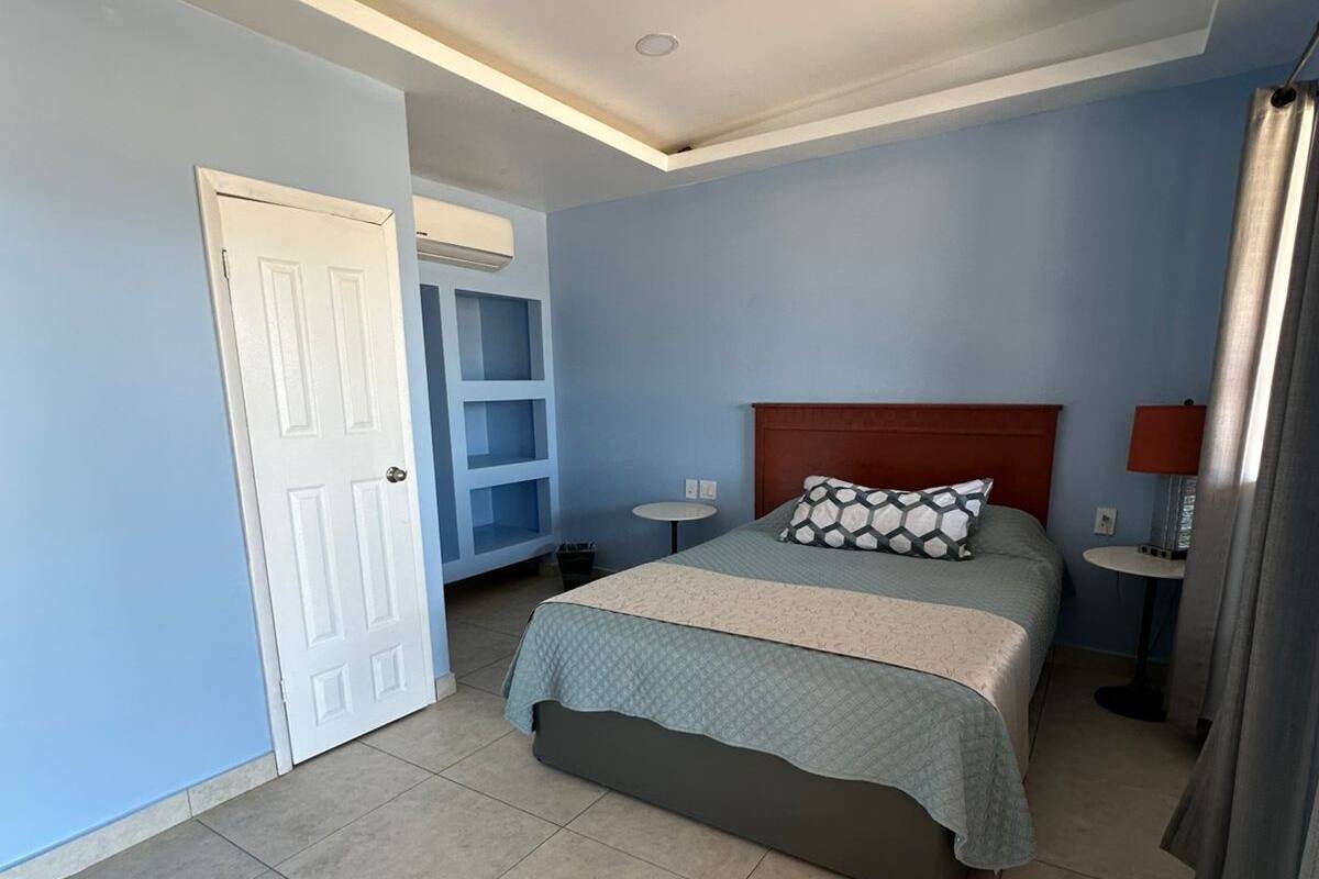 A bedroom with a bed, a ceiling fan, a door, and a small table.