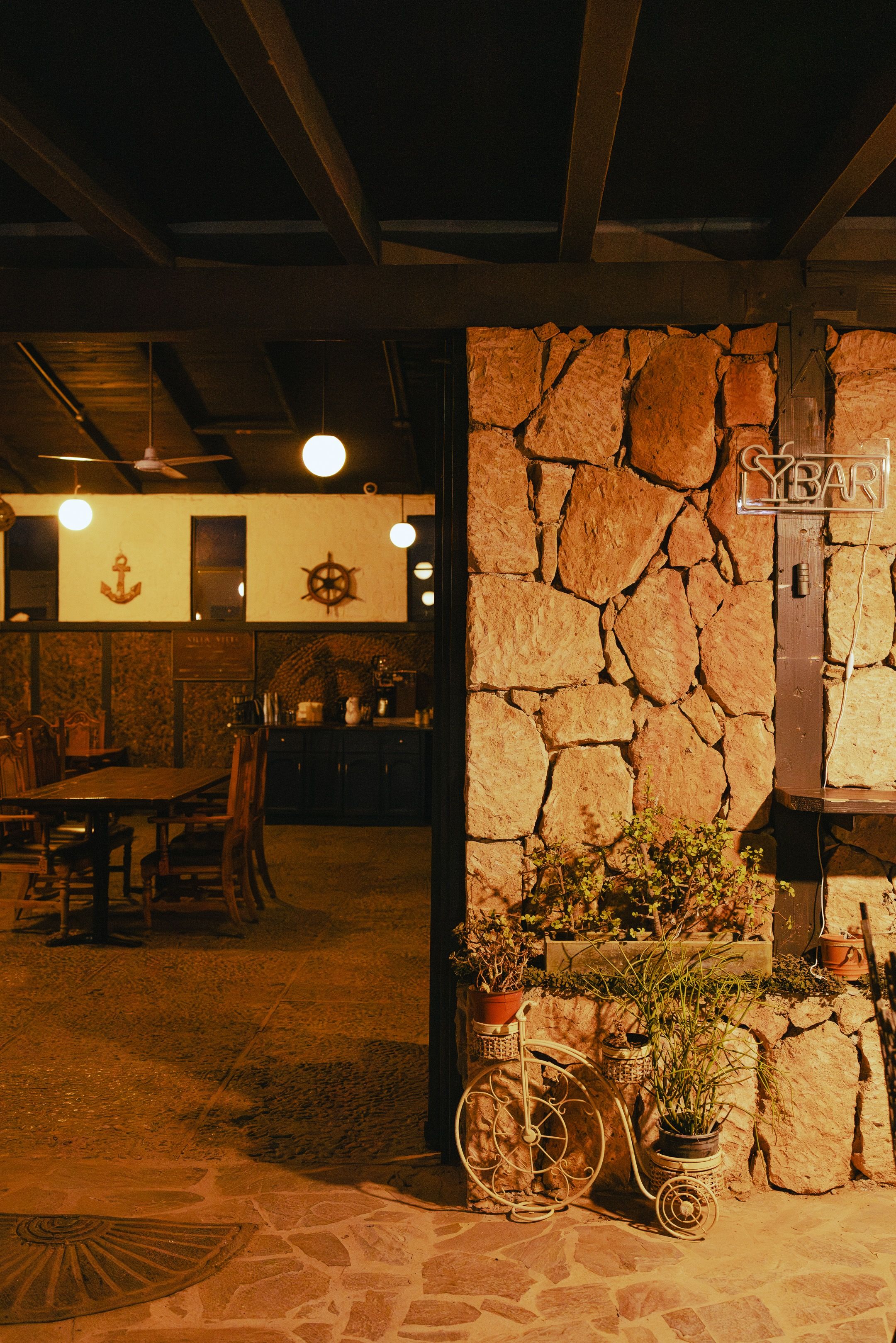 A restaurant interior with stone walls, wooden furniture, and potted plants.