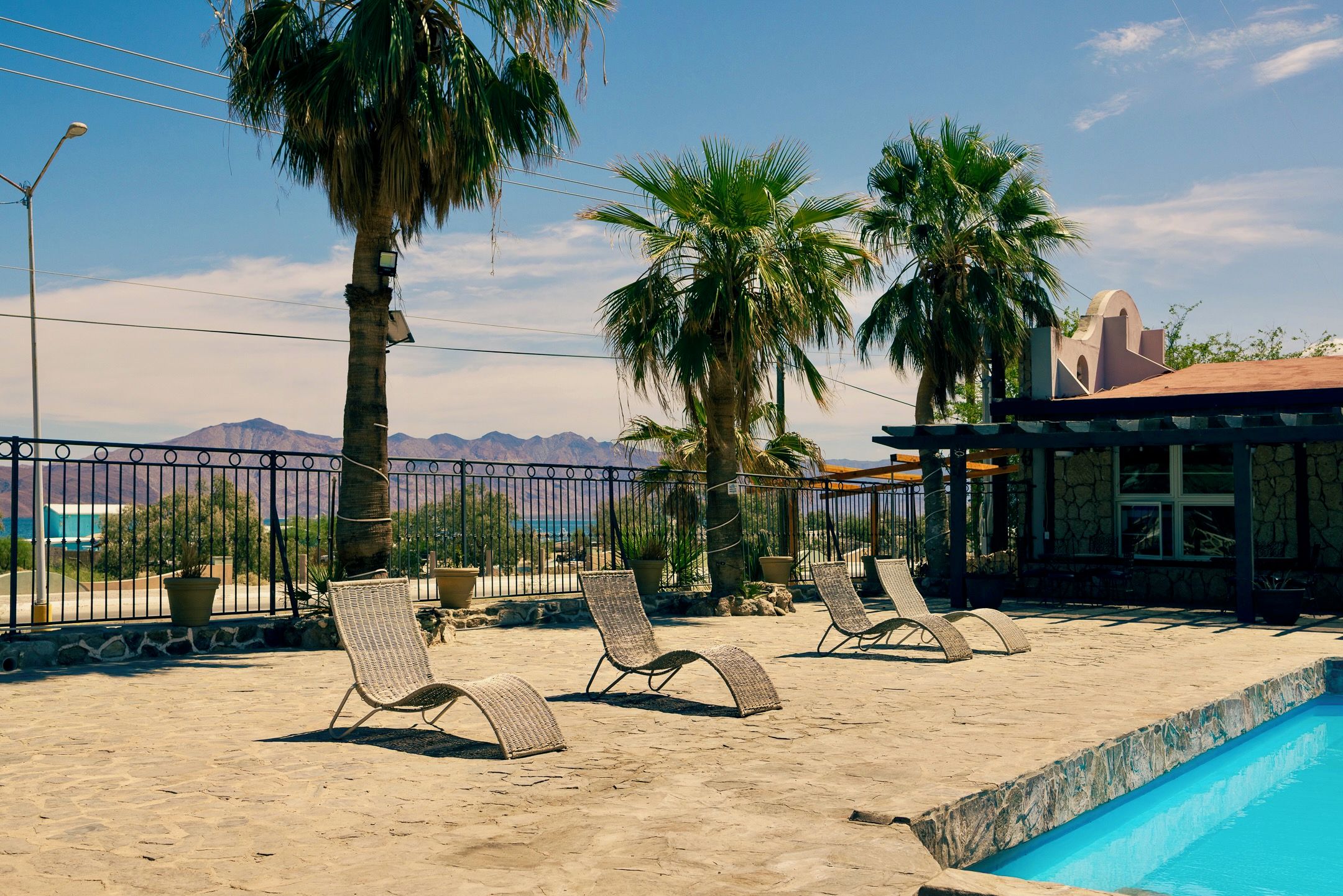 A poolside area with lounge chairs, a pool, and a view of mountains.