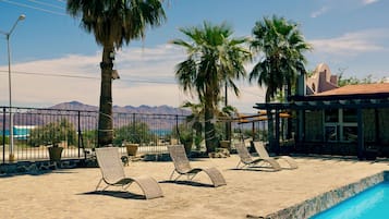A poolside area with lounge chairs, a pool, and a view of mountains.